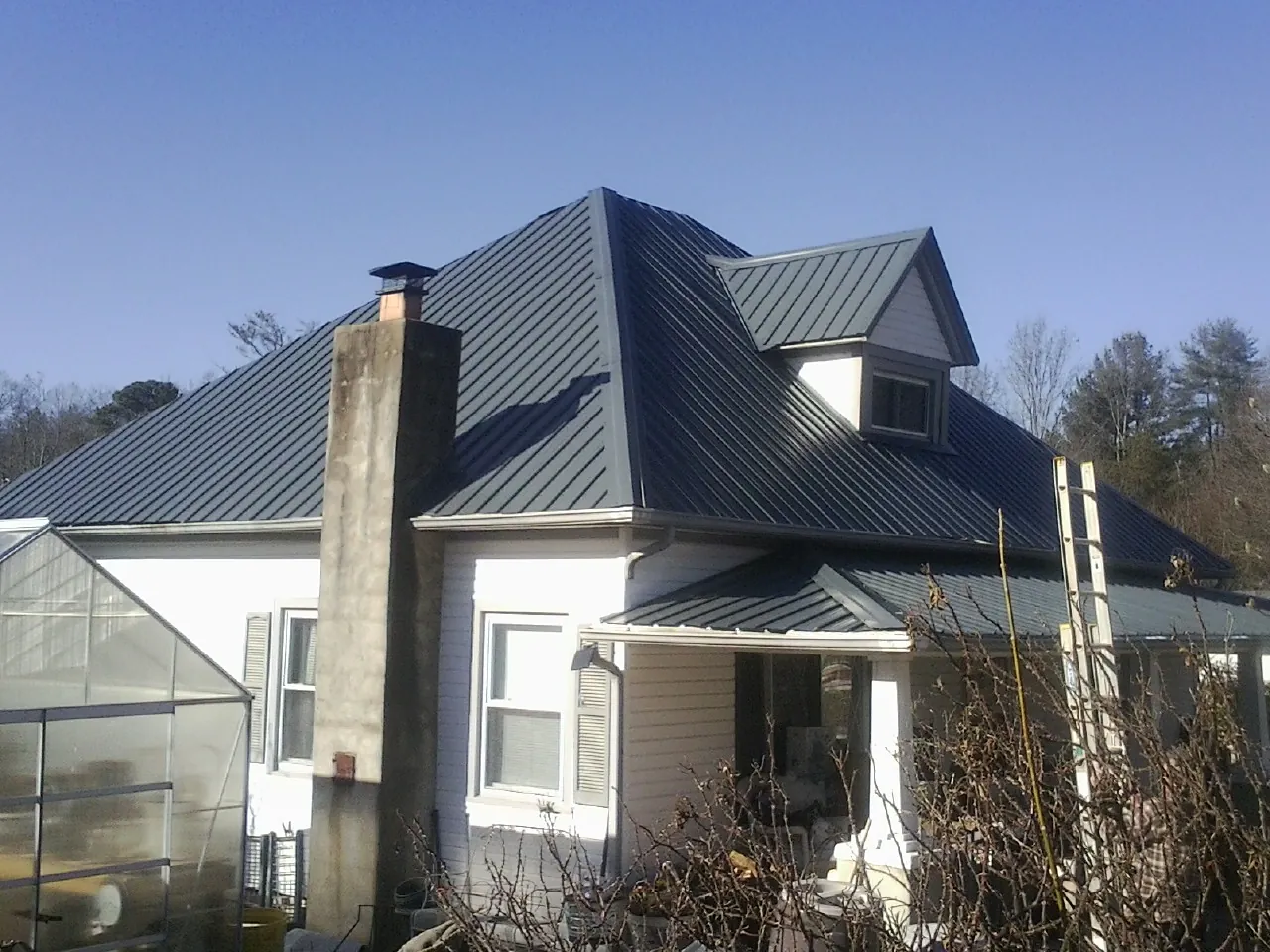 Dark blue standing seam metal roof on a white farmhouse with dormer — Slate & Tile Roof Repair by Roofing Brothers in Thornton