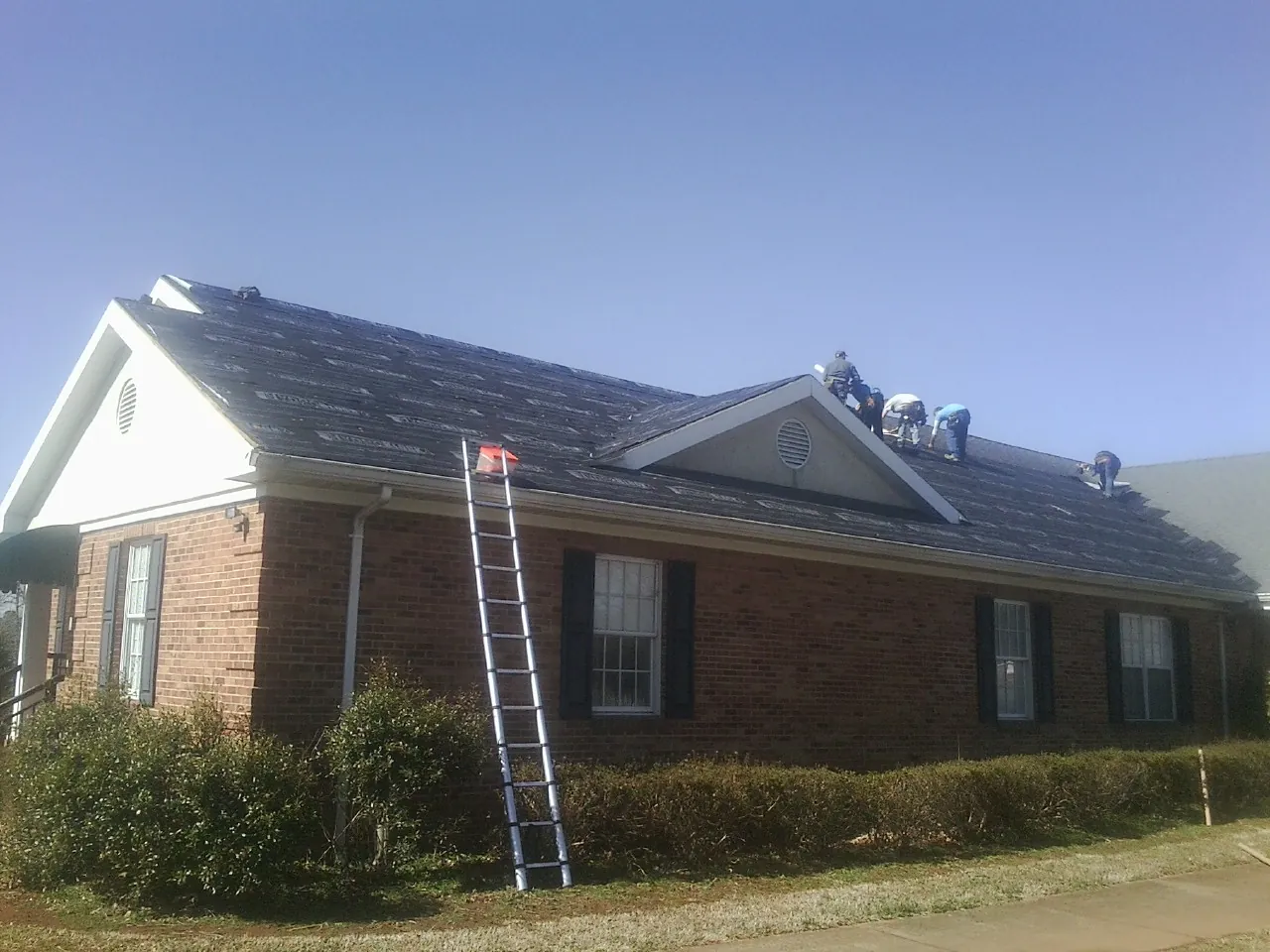 Crew tearing shingles off a brick ranch roof with a ladder set — Metal Roof Repair work by our crew in Thornton