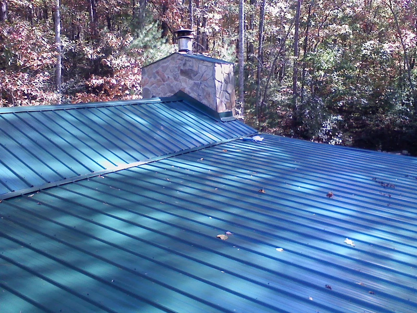 New green metal roof and stone chimney surrounded by autumn woods in Thornton